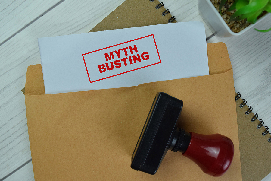 Concept of Red Handle Rubber Stamper and Myth Busting text above Brown envelope isolated on Wooden Table. Acumatica implementation myths.