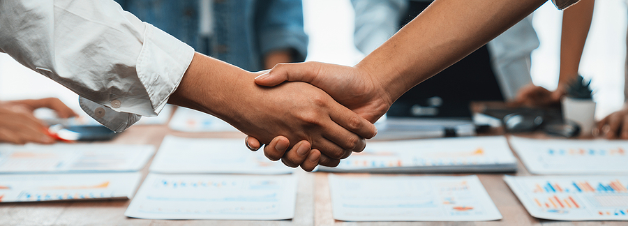 Analyst team celebrates successful data analysis with handshake. Panorama shot handshaking after adjusting attitude or brainstorm for future success in meeting room with BI dashboard paper.